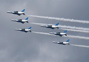 曇り空のなかスモークを出しながら飛ぶ6機のブルーインパルス